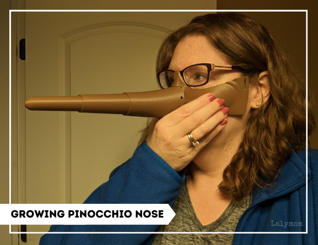 photo of a woman holding an unpainted brown Pinocchio mask on her face. 